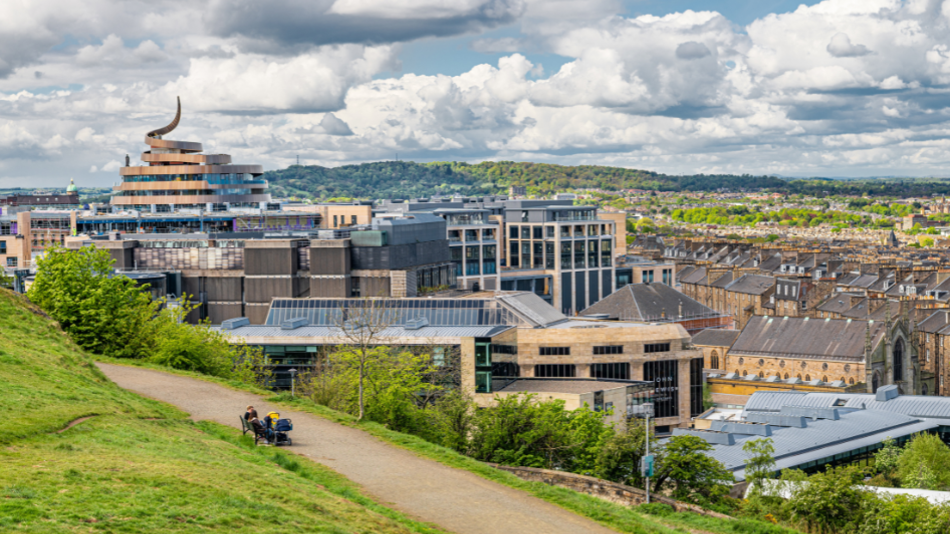 View from park over city location with retail, office and residential buildings. People sitting on a bench in the park.