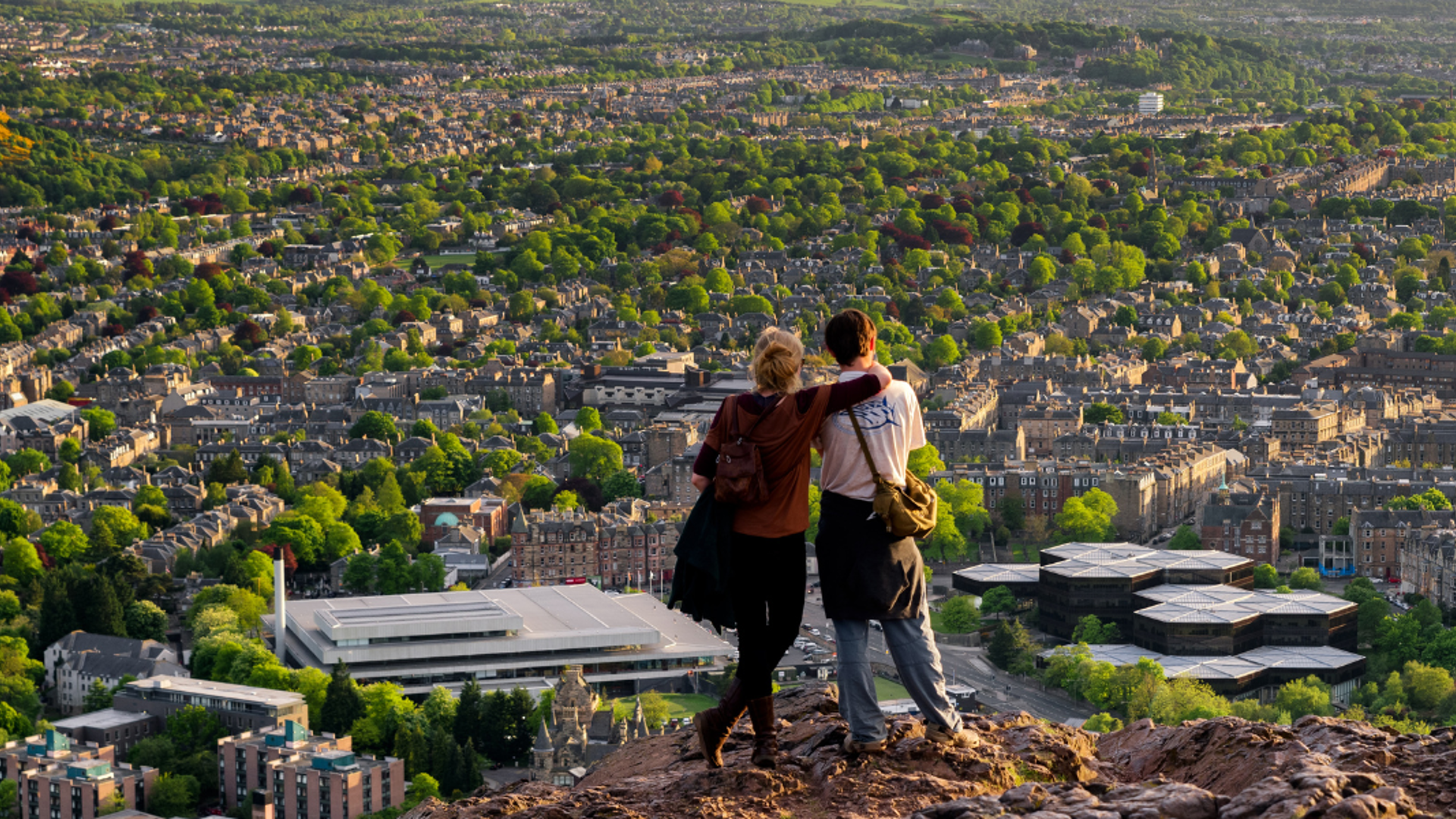 People on a hill overlooking a city with lots of trees and grassland.