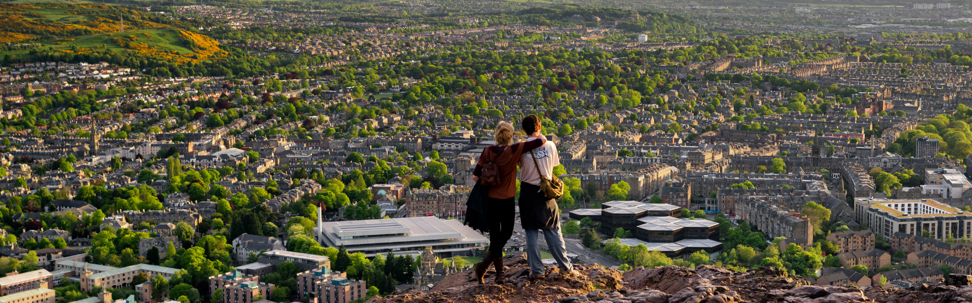 People on a hill overlooking a city with lots of trees and grassland.